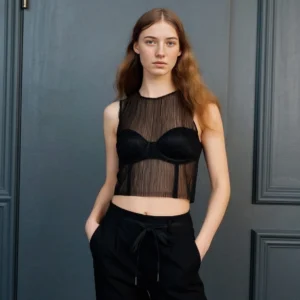 Une femme portant un haut en dentelle noire et un pantalon noir debout devant une porte, générée et modifiée avec PiktID genAI